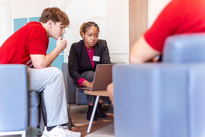 two students speak with a professor in the library